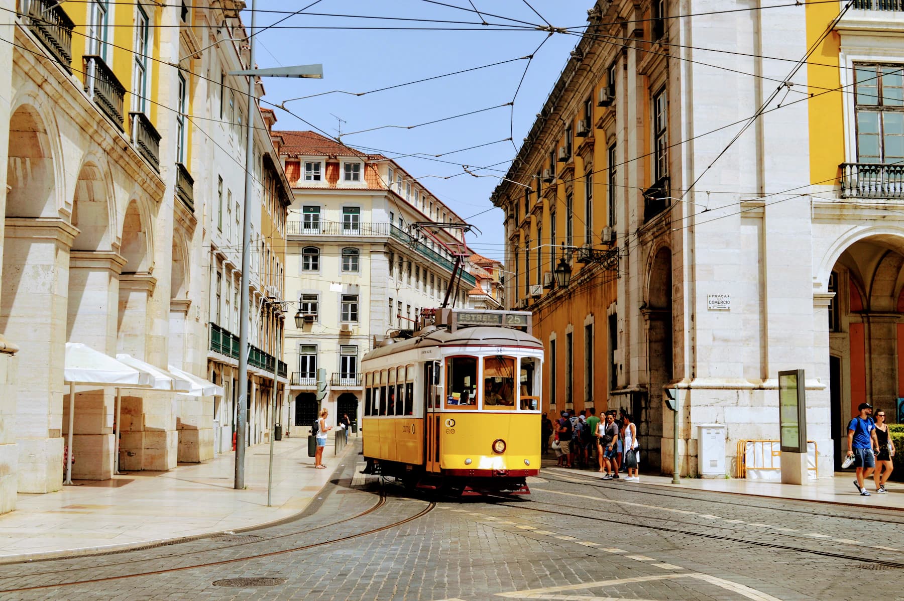 A yellow tram travels through a street of historic buildings in Lisbon